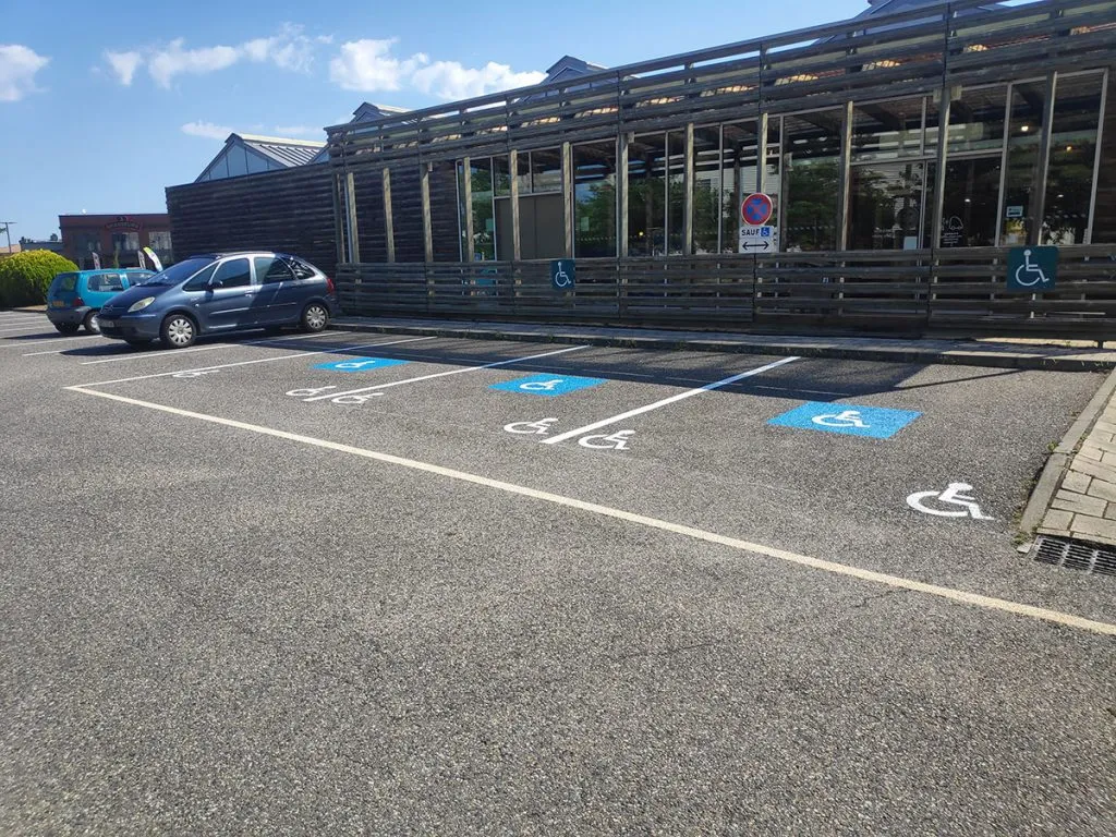 Quatre places de stationnement PMR avec pictogrammes bleus devant un commerce