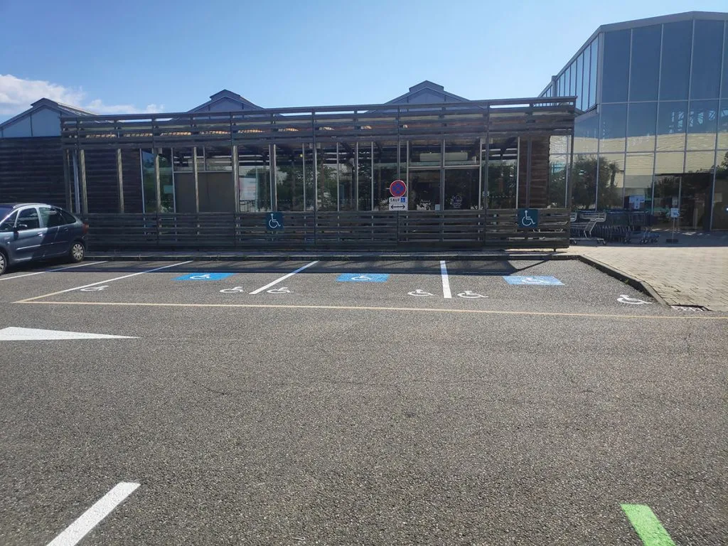 Rangée de places réservées avec pictogrammes au sol et panneaux devant un commerce