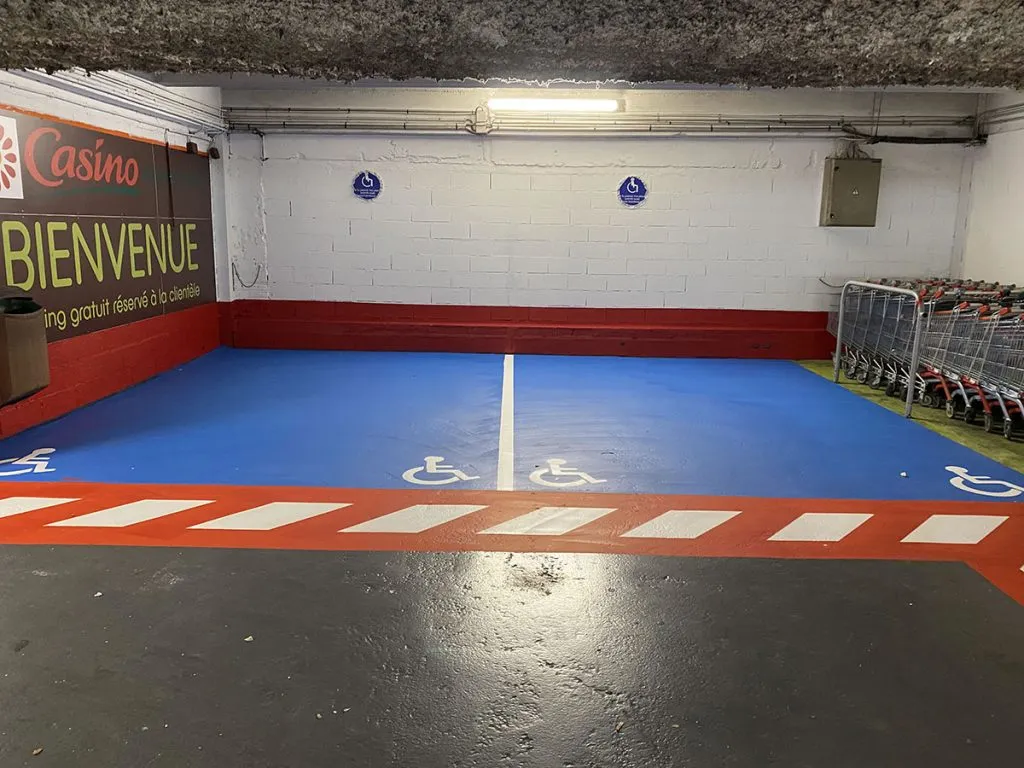 Place PMR bleue avec pictogramme blanc sur un parking de commerce
