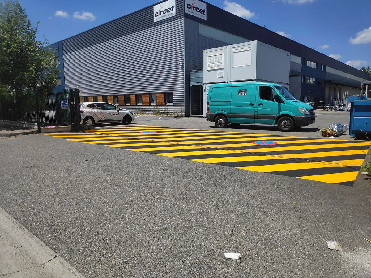 Grande zone de sécurité rayée en jaune et noir devant un bâtiment technique