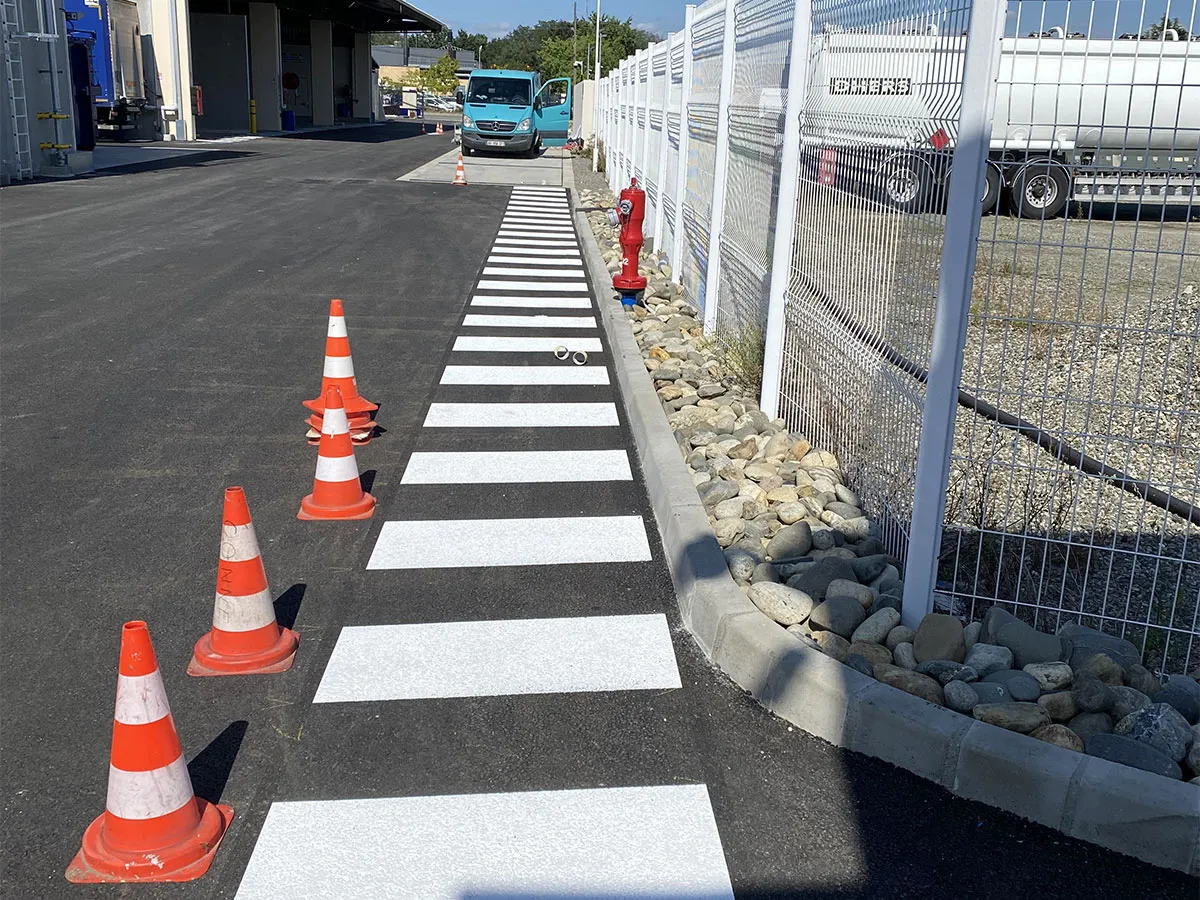 Passage piéton blanc en cours de traçage le long d’une clôture