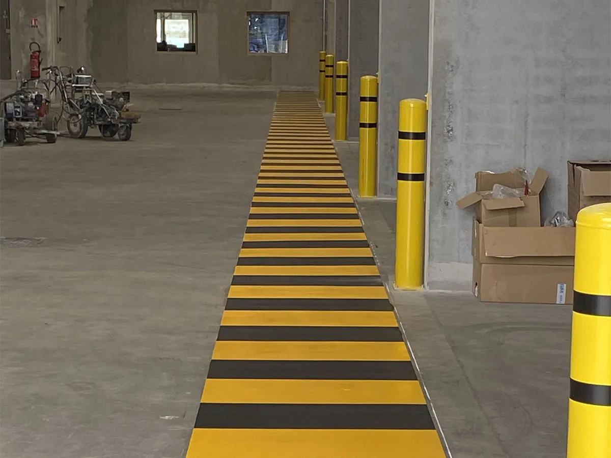 Passage piéton noir et jaune reliant les circulations d’un site industriel