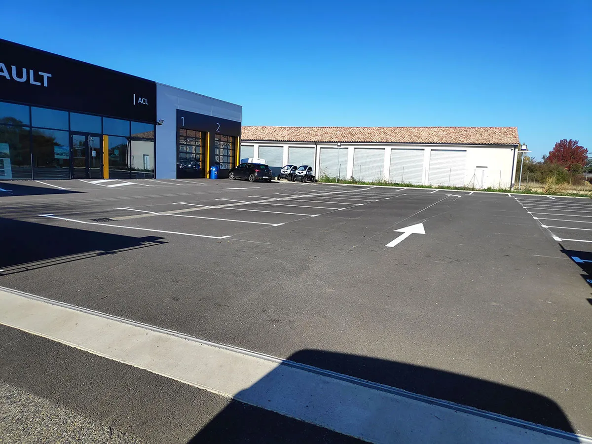 Parking professionnel avec lignes blanches et flèche de circulation devant une concession automobile