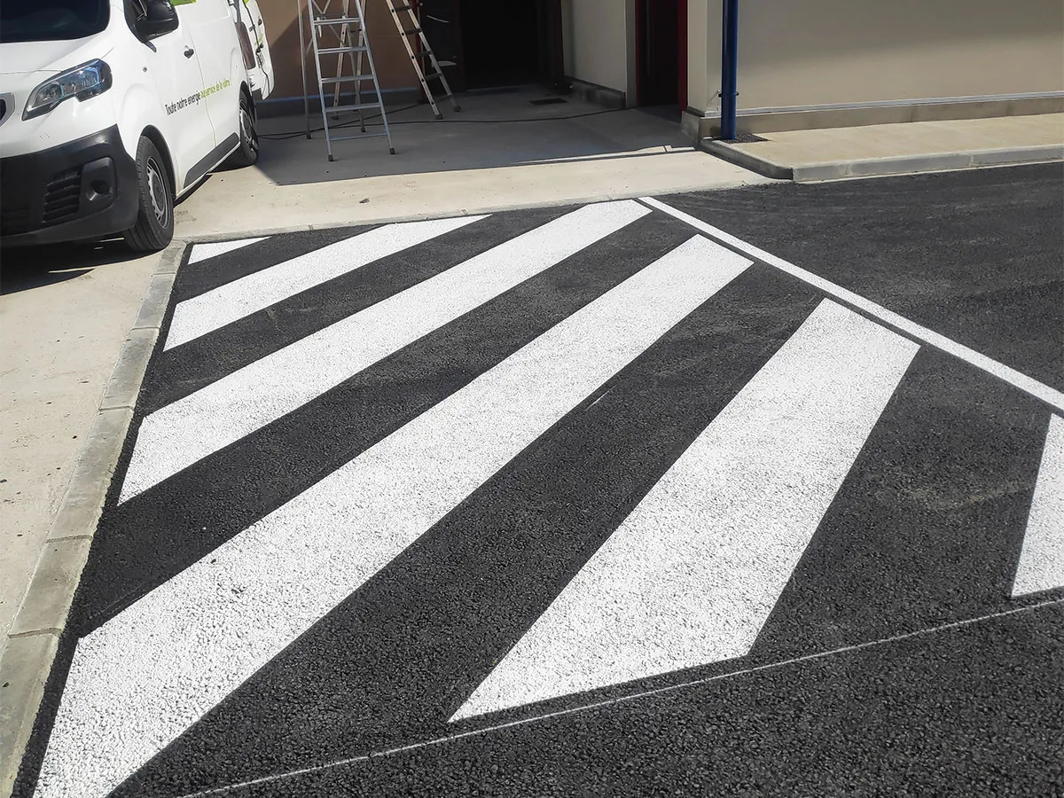 Zone de circulation professionnelle avec zébra blanc tracé devant un portail